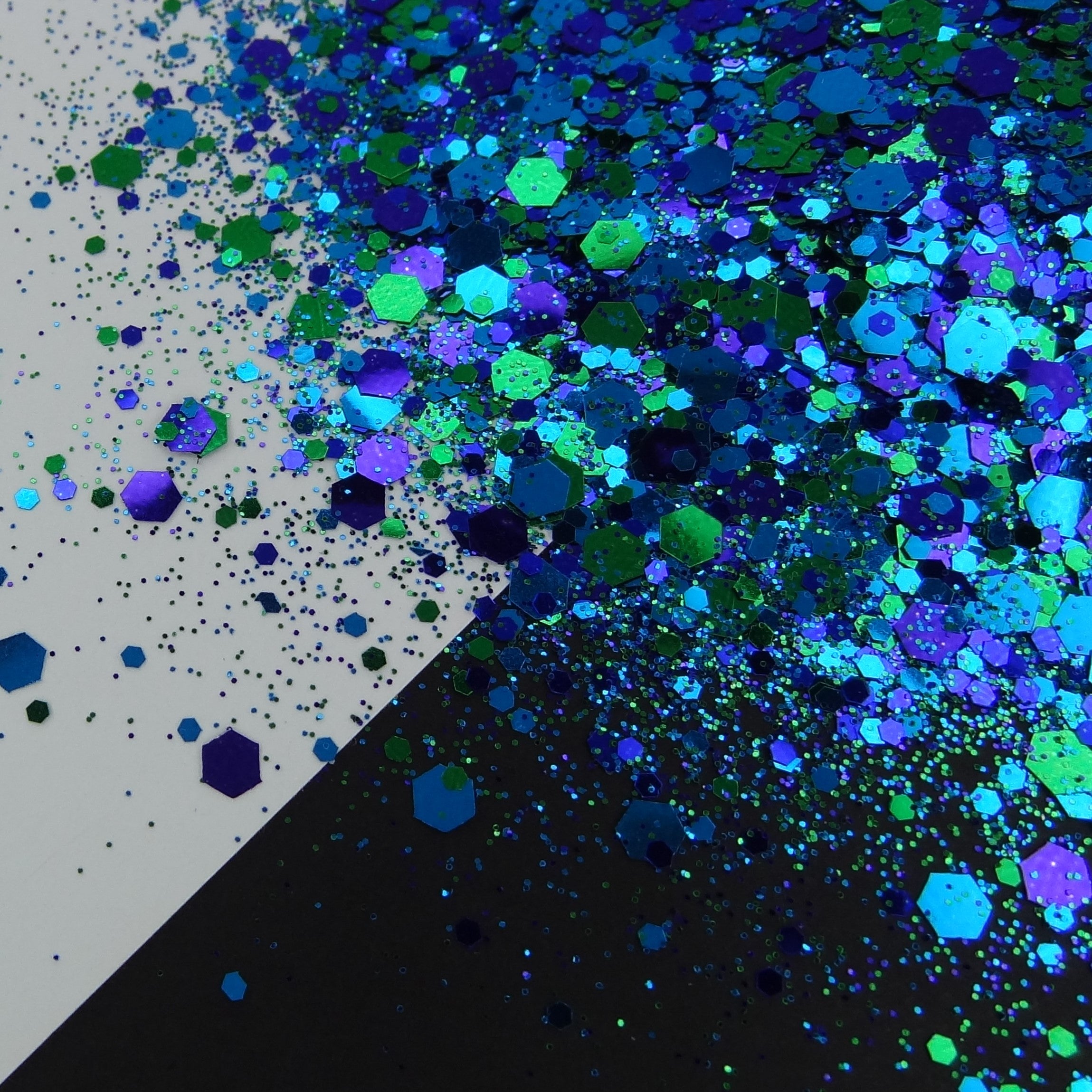 A blue and green chunky glitter mix spread out on a black and white background.