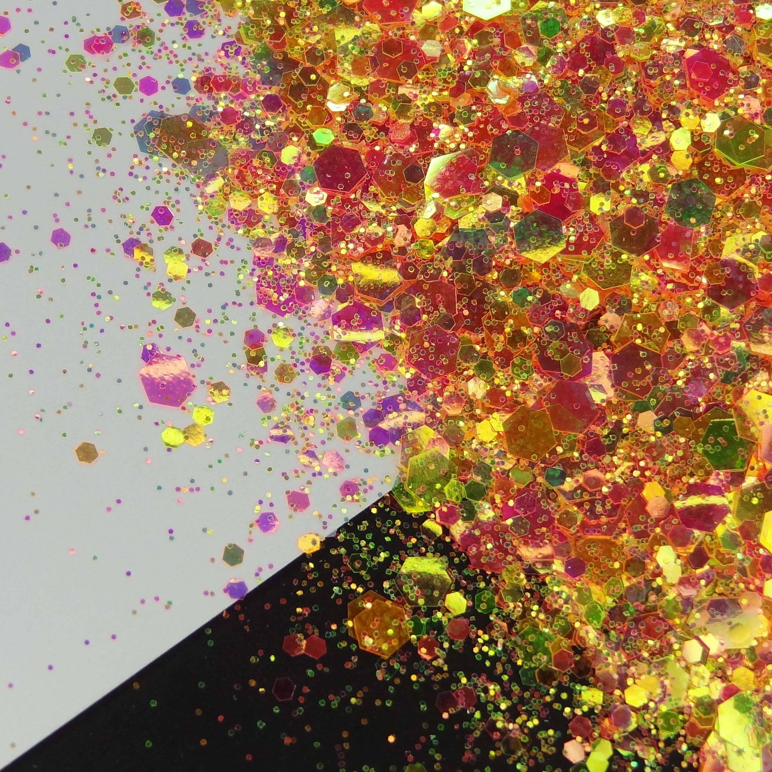 A pile of mixed colours of chunky glitter, including Orange/Pink/Green/Coral on a white and black background.