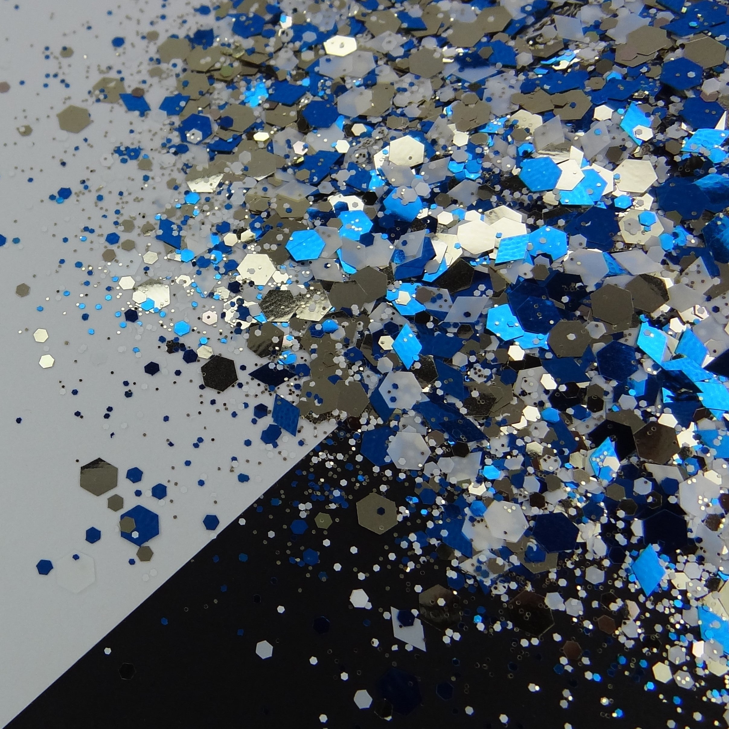 A pile of mixed colours of chunky glitter,  including Blue/White/Gold on a white and black background.