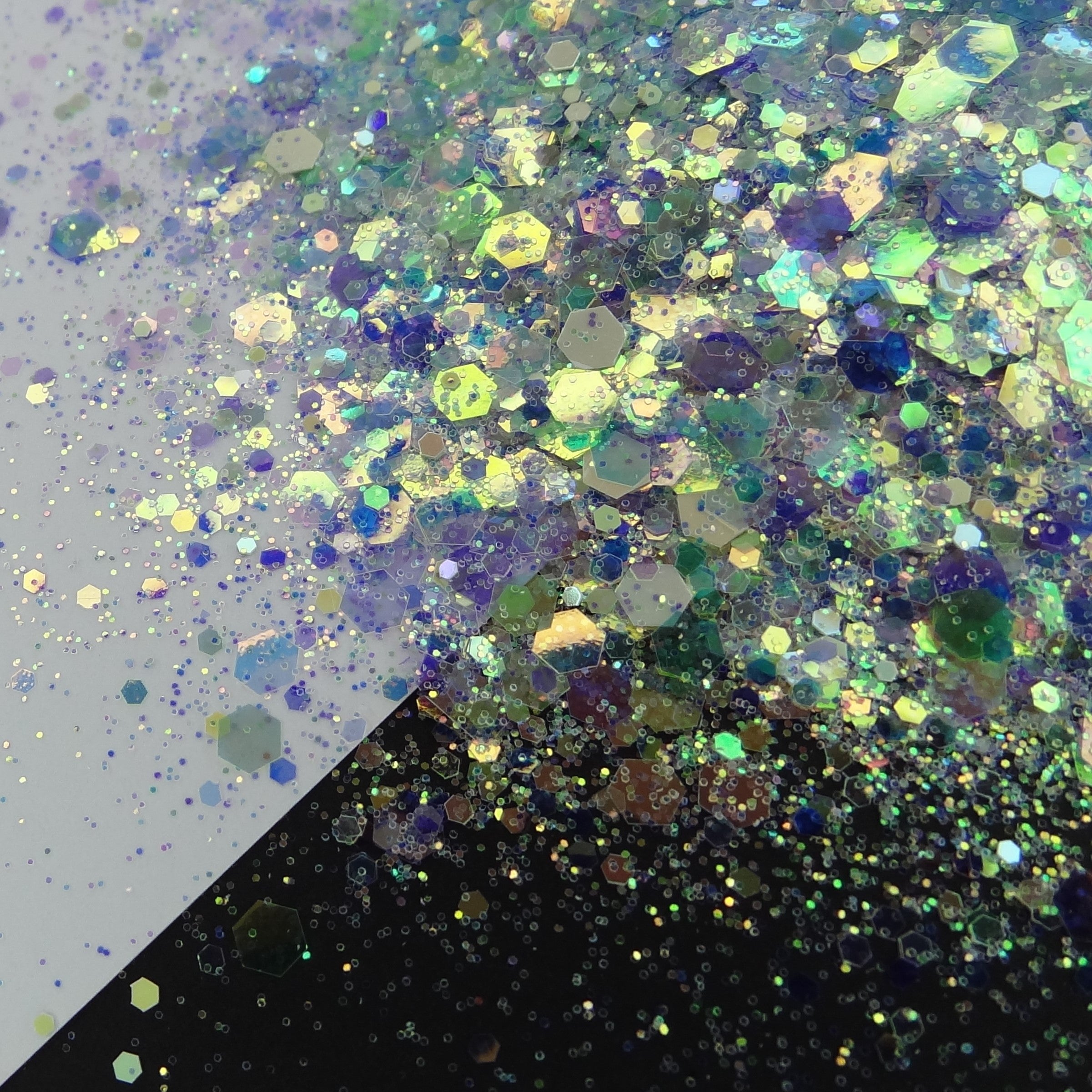 A pile of mixed colours of chunky glitter, including White/Green/Mint/Purple/Blue on a white and black background.