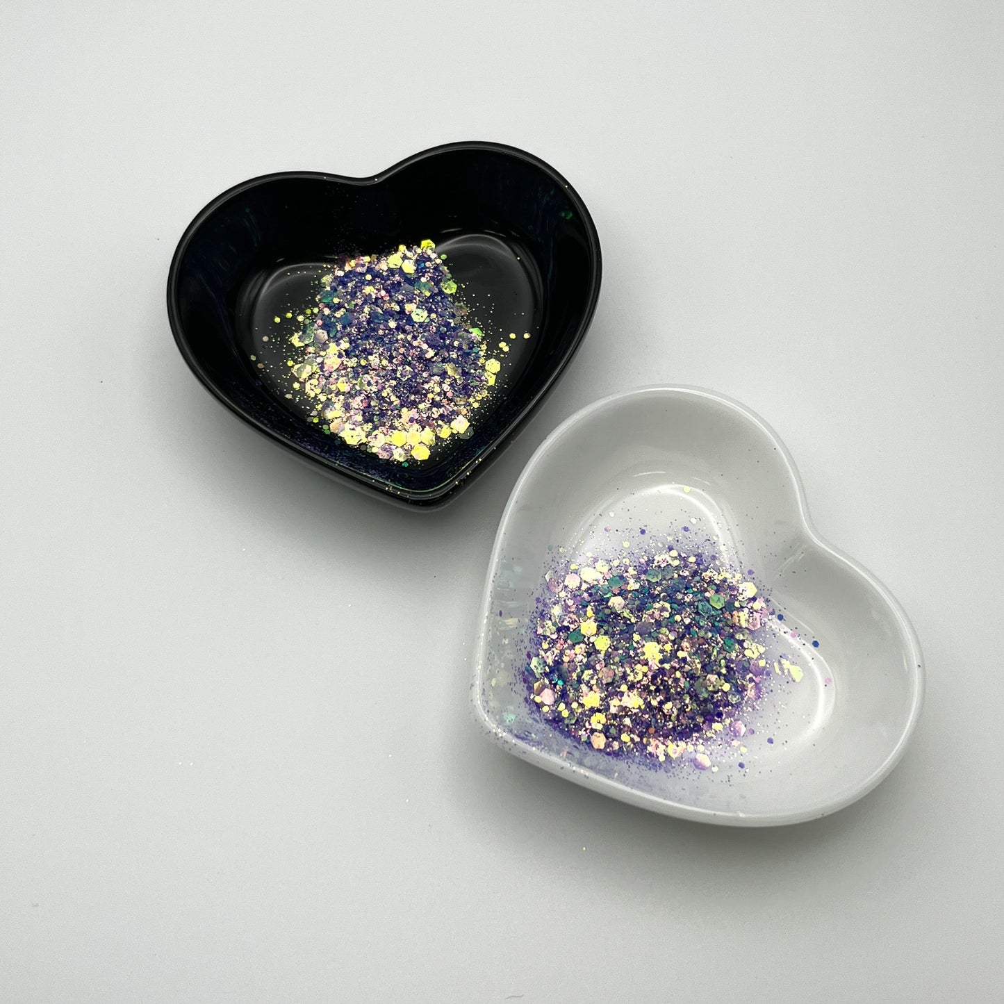 Two heart-shaped dishes, one black and one white, containing purple chunky glitter.