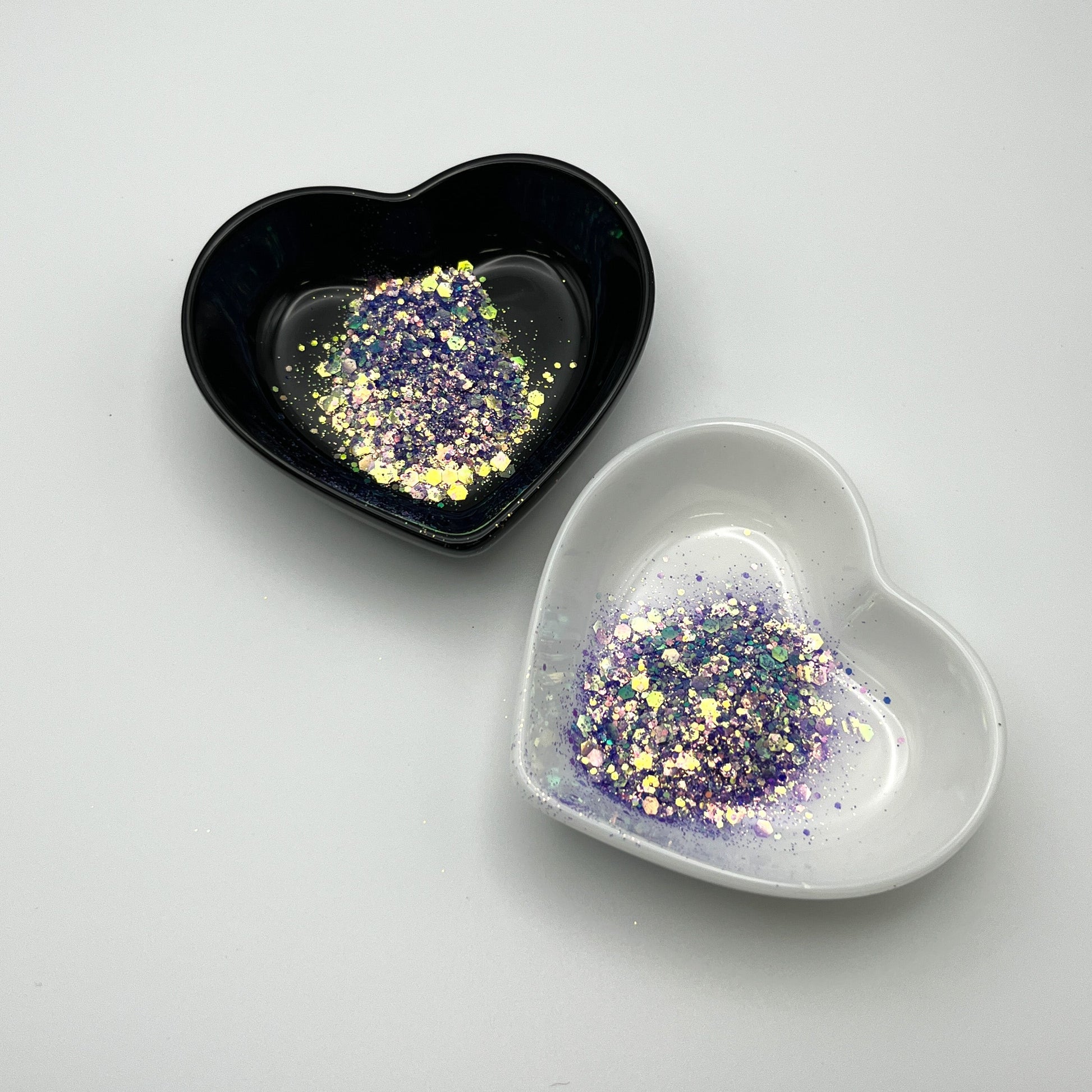 Two heart-shaped dishes, one black and one white, containing purple chunky glitter.