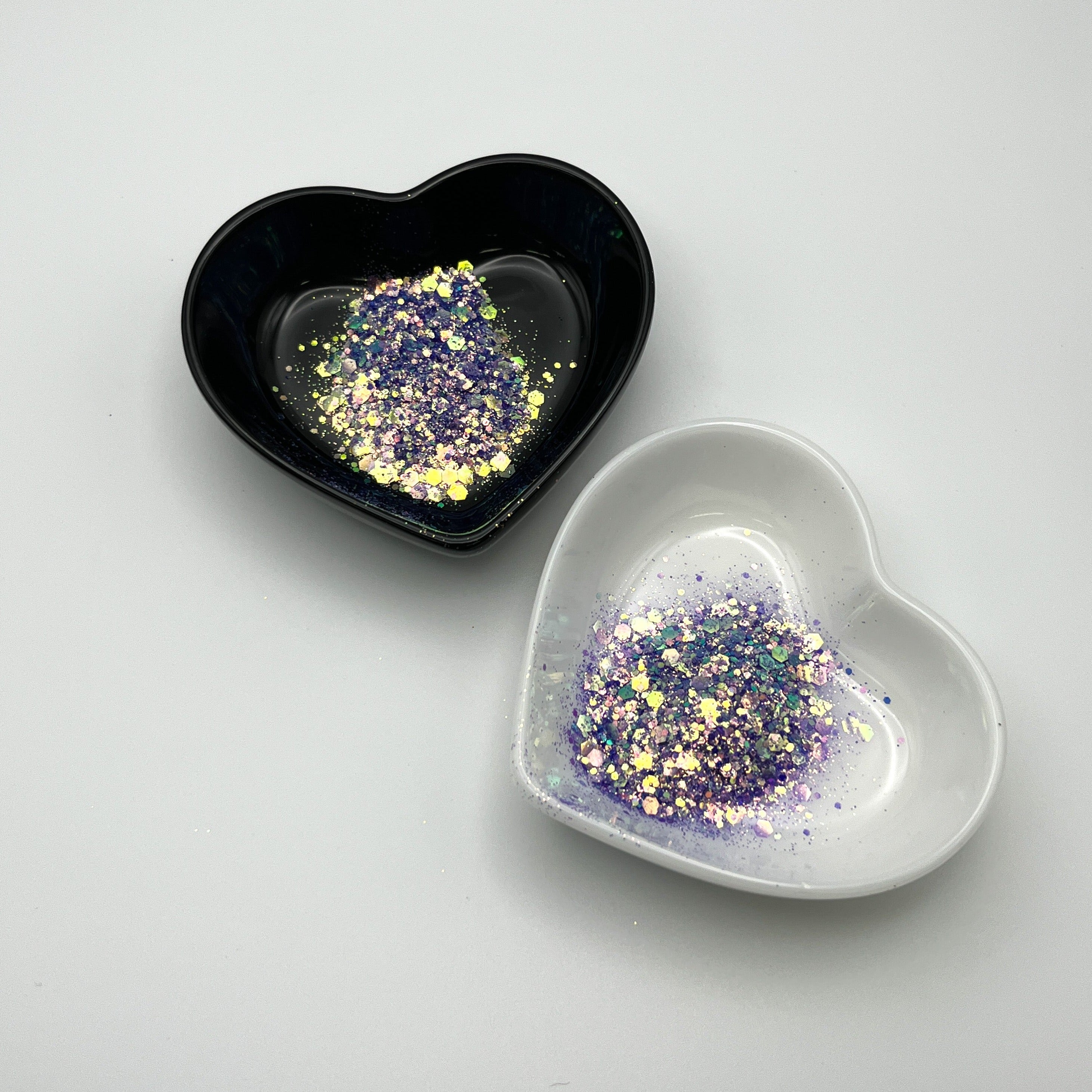 Two heart-shaped dishes, one black and one white, containing purple chunky glitter.