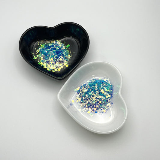 Two heart-shaped dishes, one black and one white, containing blue chunky glitter.