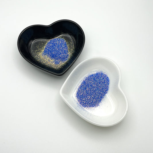 Two heart-shaped dishes, one black and one white, containing blue extra fine glitter.
