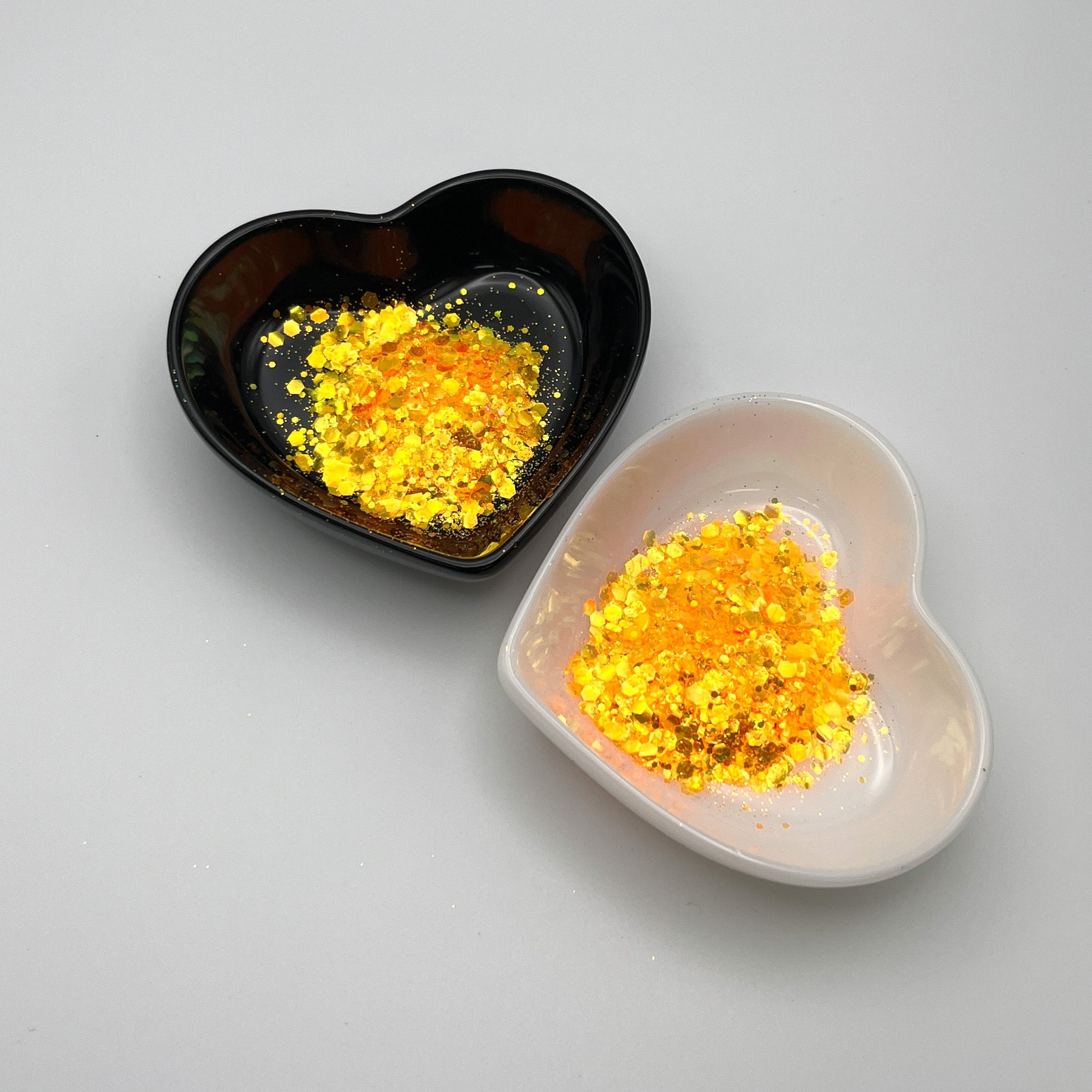 Two heart-shaped dishes with orange colored glitter spread out, one dish is black and the other is white.