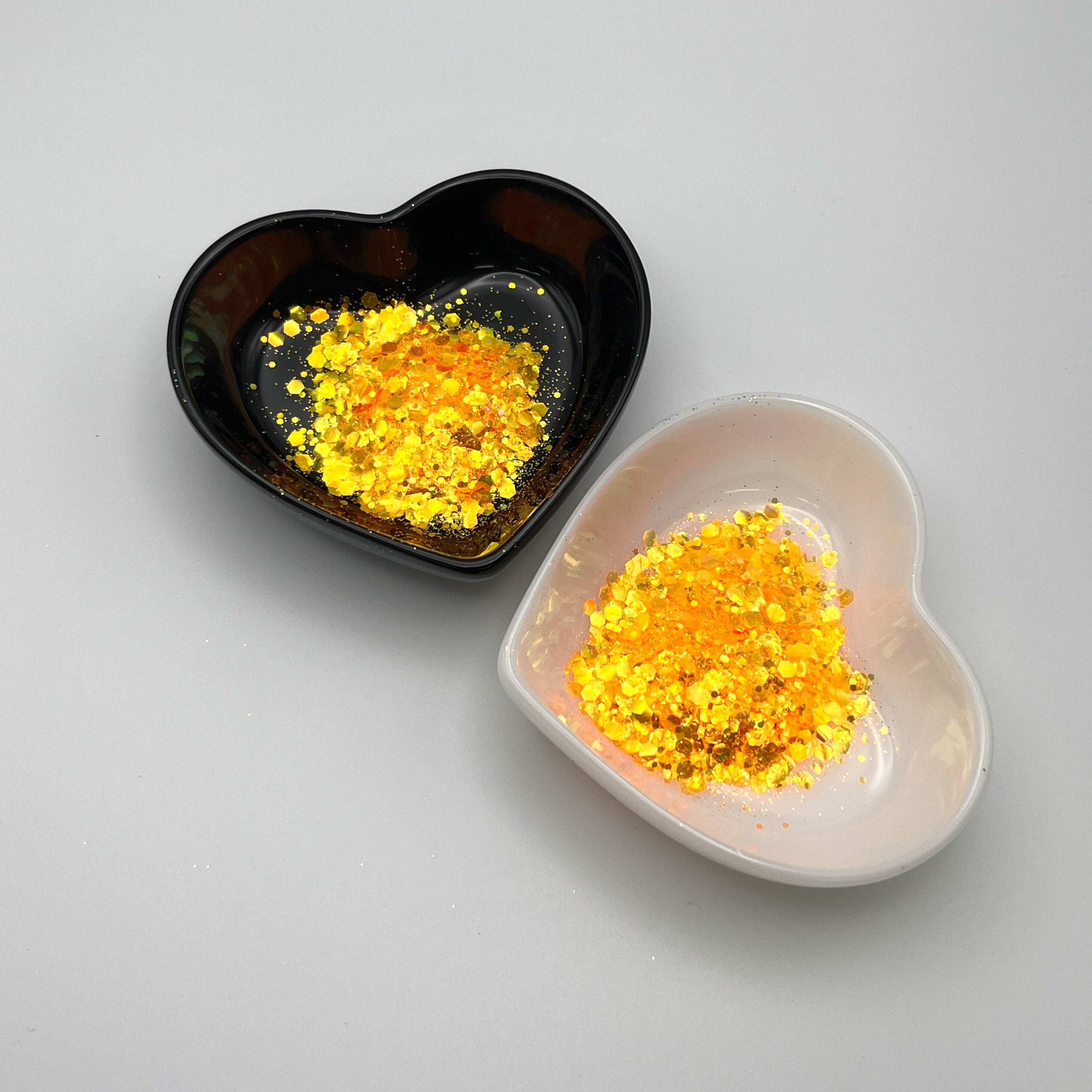 Two heart-shaped dishes with orange colored glitter spread out, one dish is black and the other is white.