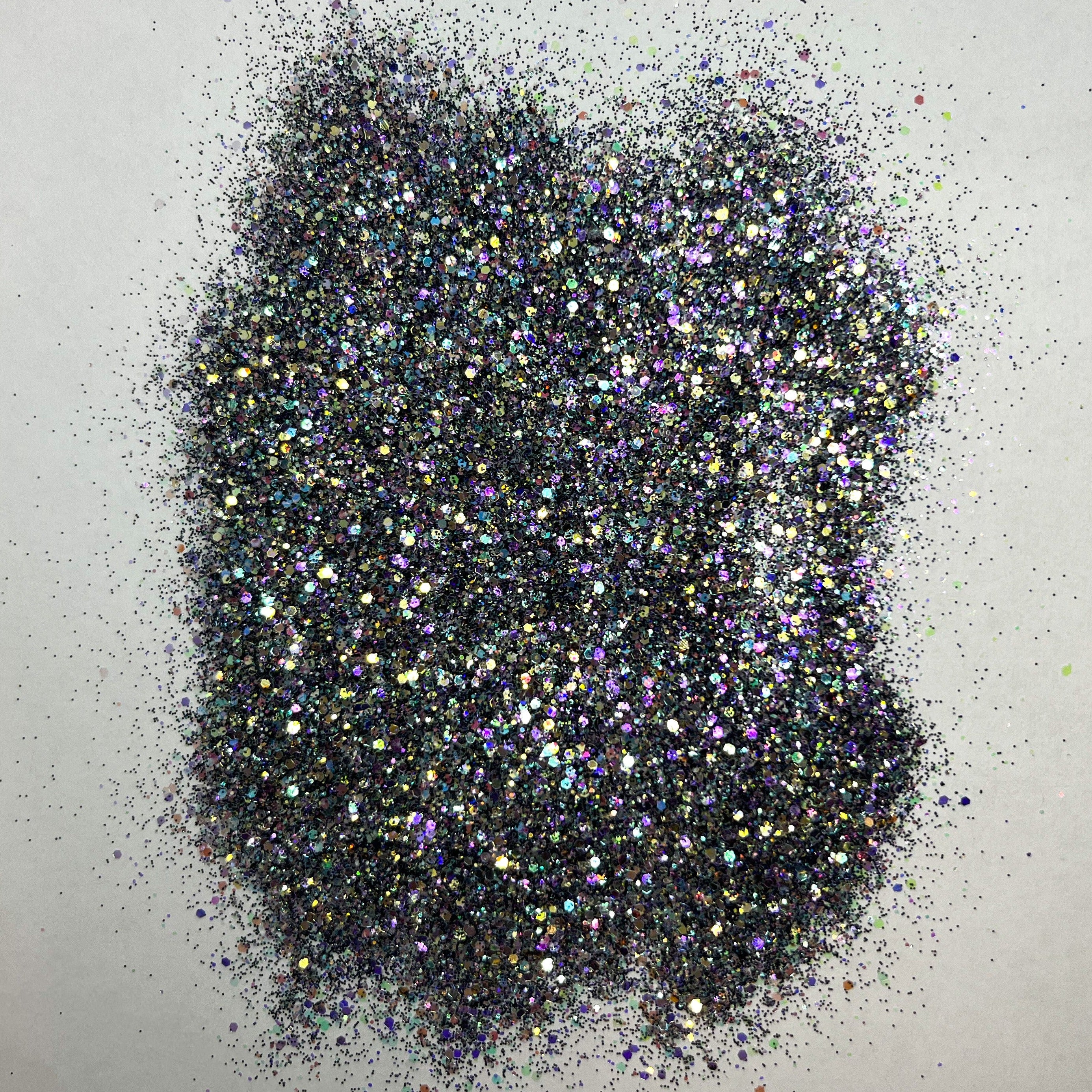 A pile of multicolored glitter, with a predominance of black hues, spread out on a surface.
