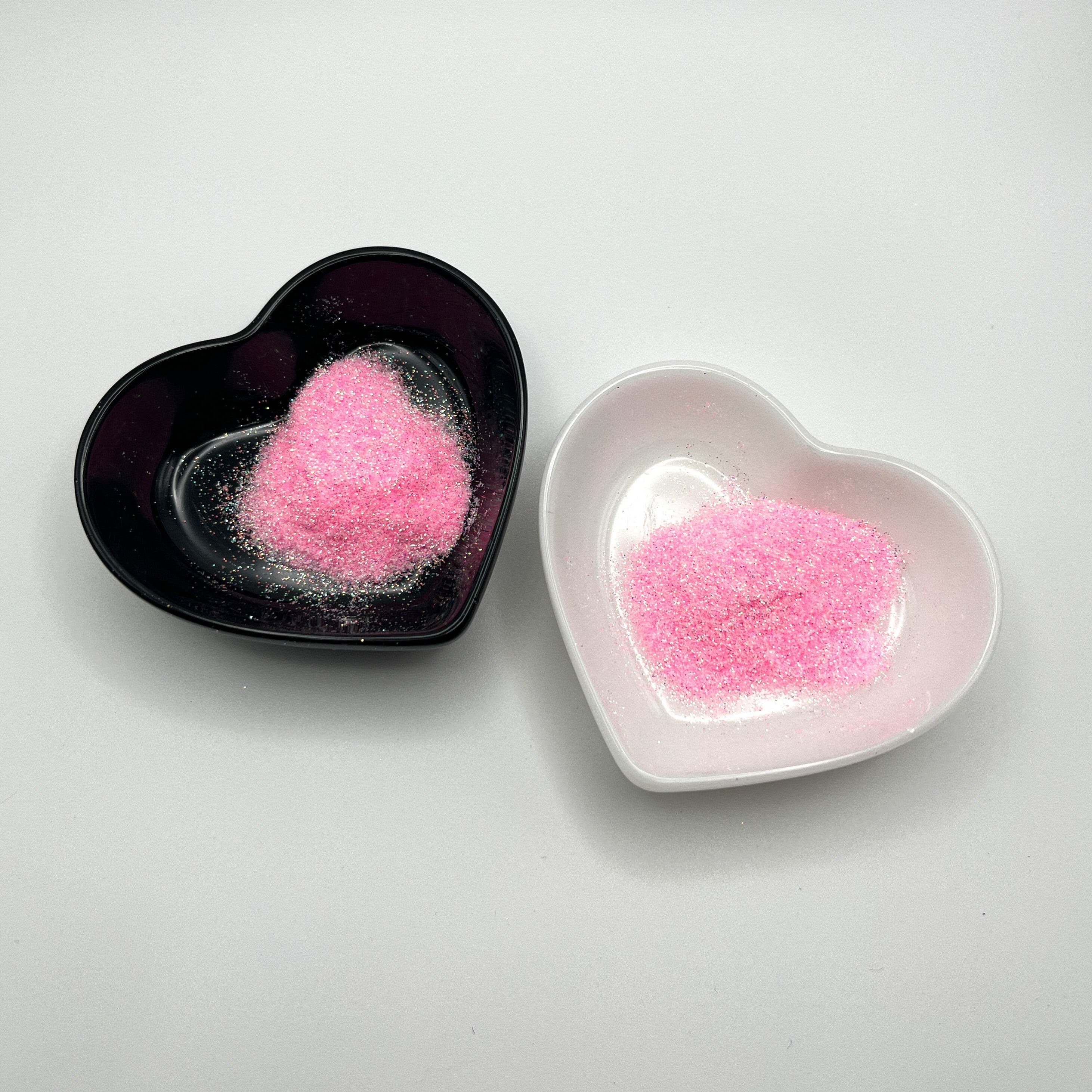 Two heart-shaped dishes, one black and one white, both containing pink extra fine glitter.