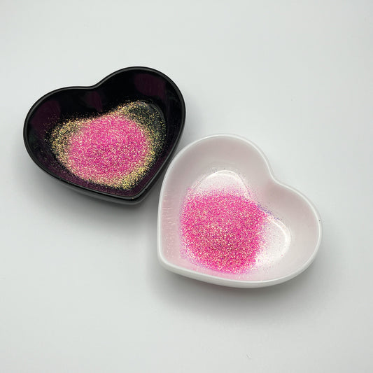 Two heart-shaped dishes, one black and one white, both containing light pink extra fine glitter.
