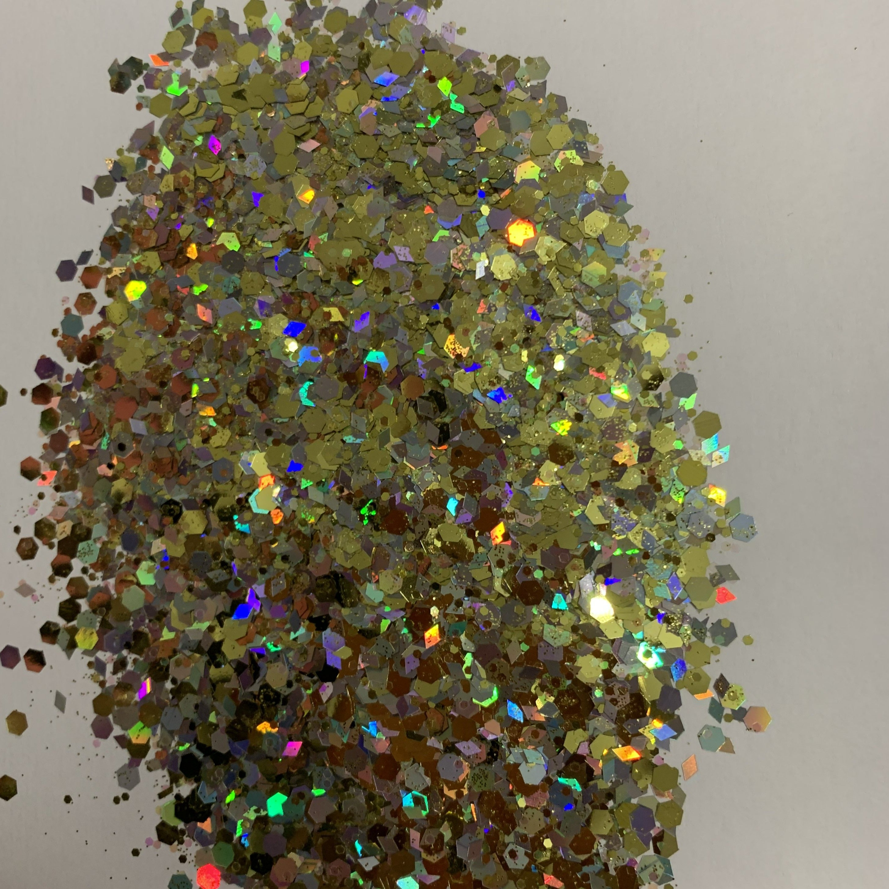 A close-up image of multicolored chunky glitter, with hues of gold, silver, and holographic reflective surfaces.