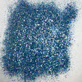 A pile of multicolored glitter, with a predominance of blue hues, spread out on a surface.