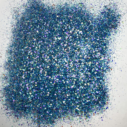 A pile of multicolored glitter, with a predominance of blue hues, spread out on a surface.