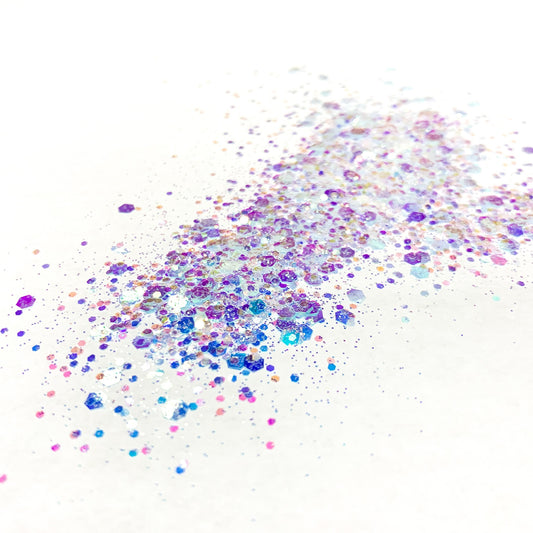 A scattered glitter mix of various sizes with colors ranging from white reflecting, blue, pink, to purple on a white background.