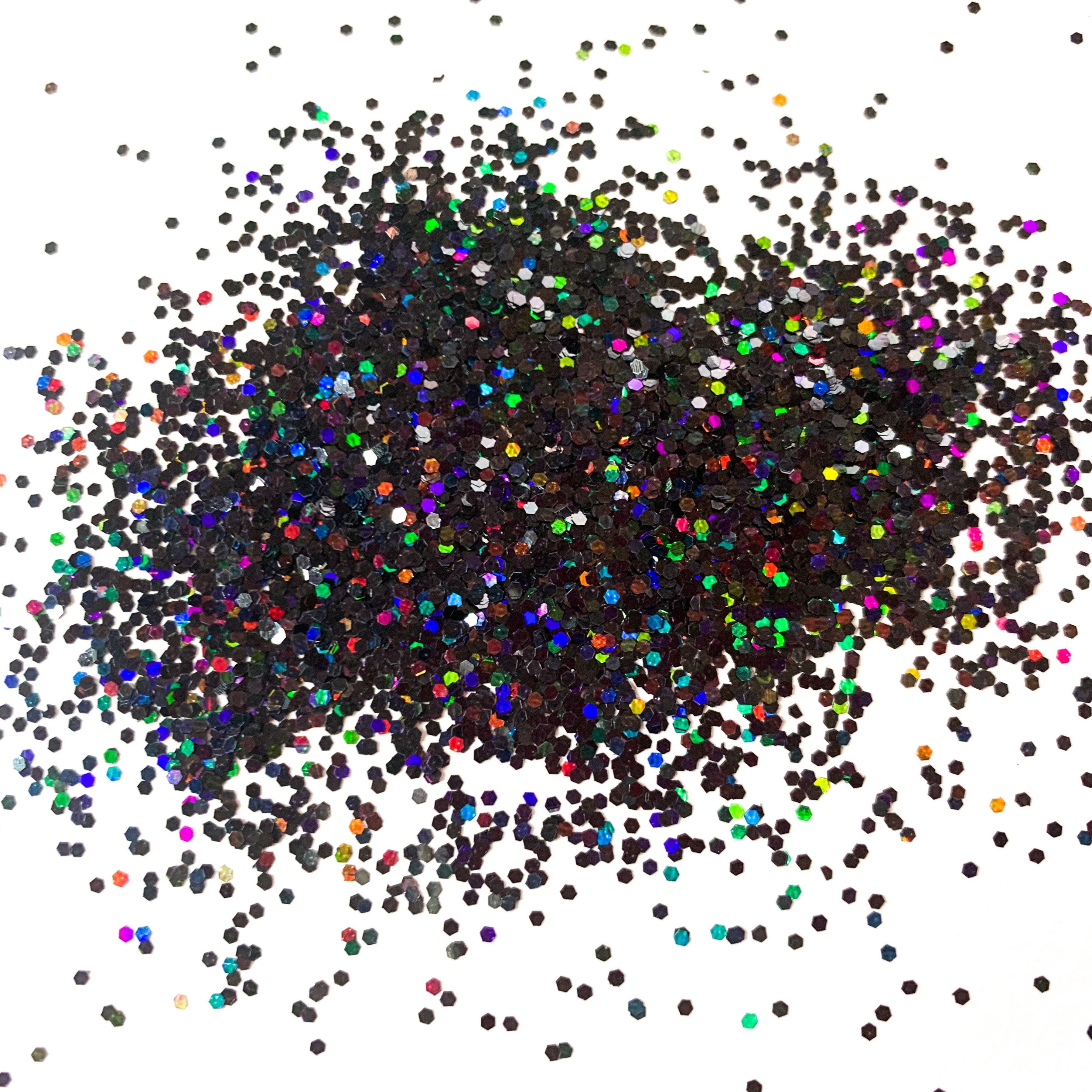 A pile of multicolored glitter particles, ranging from black to various shades of multicolor, spread out on a white background.