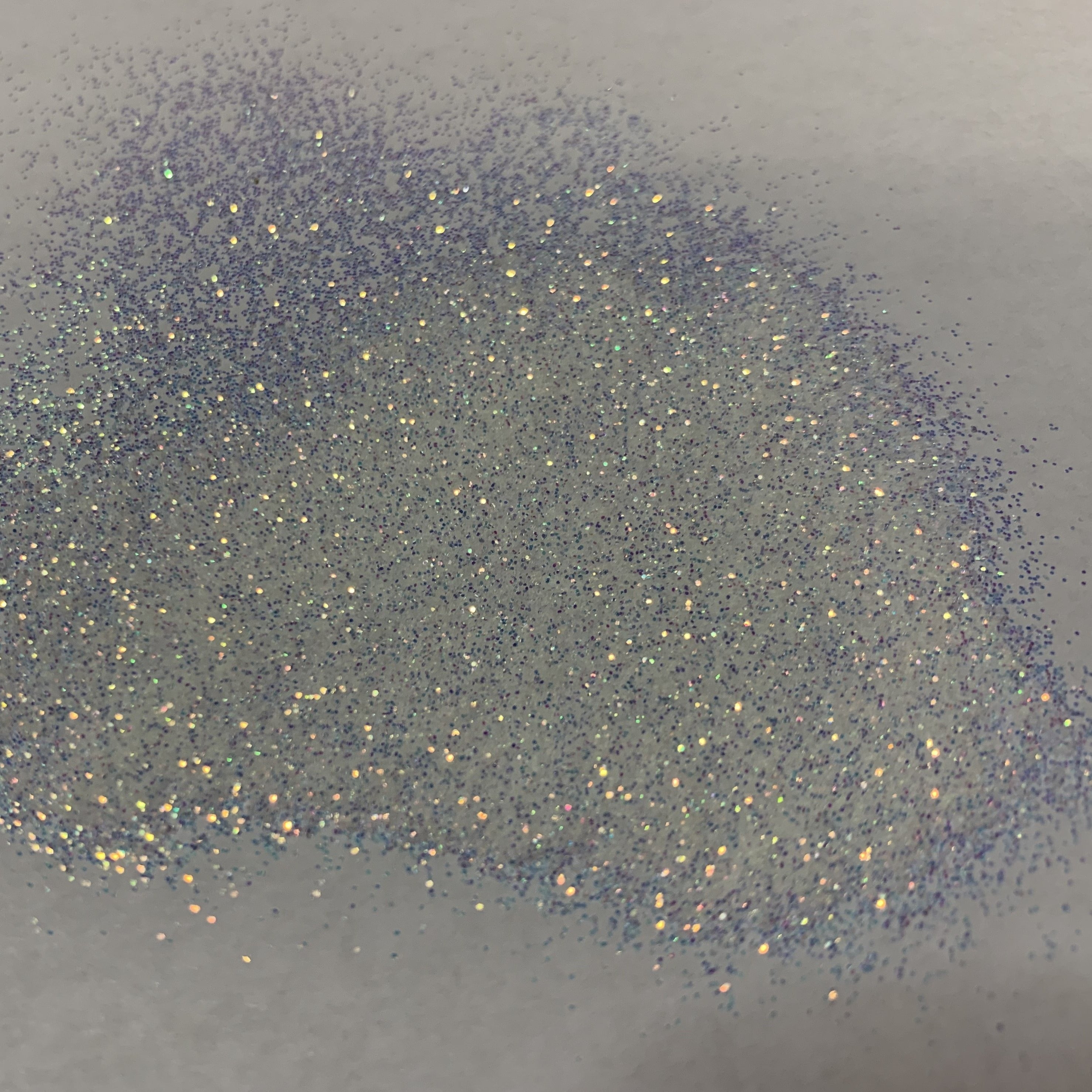 A close-up image of extra fine opal glitter spread on a surface, showing the glitter's iridescent properties and the true color of the product.