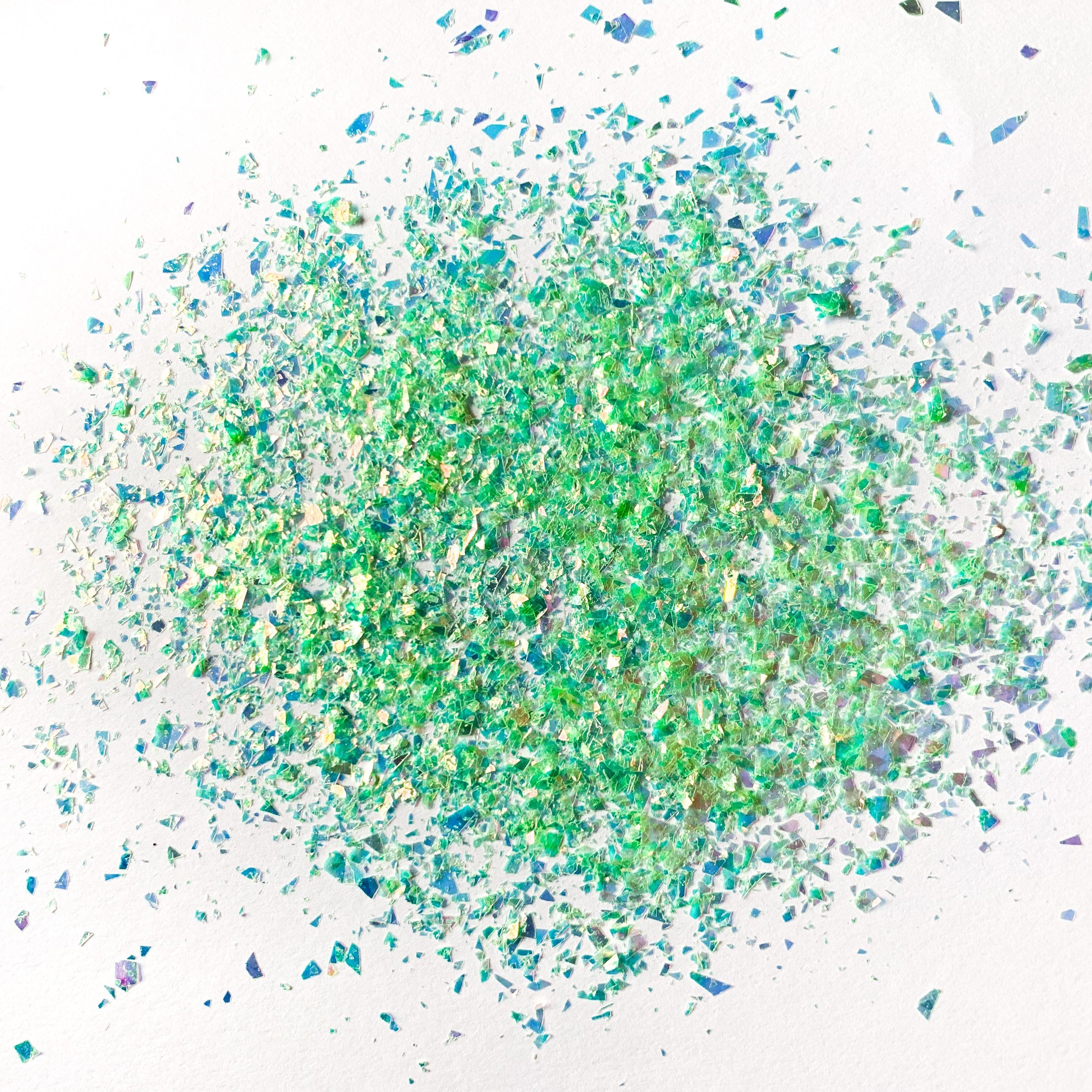 A pile of green irregular glitter flakes spread out on a white background.