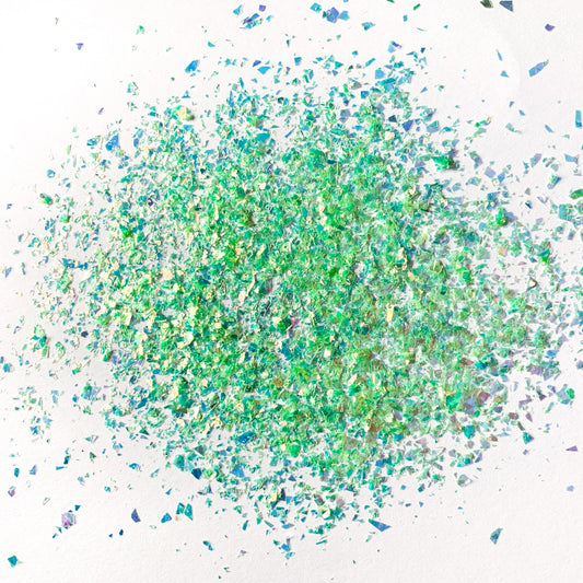 A pile of green irregular glitter flakes spread out on a white background.