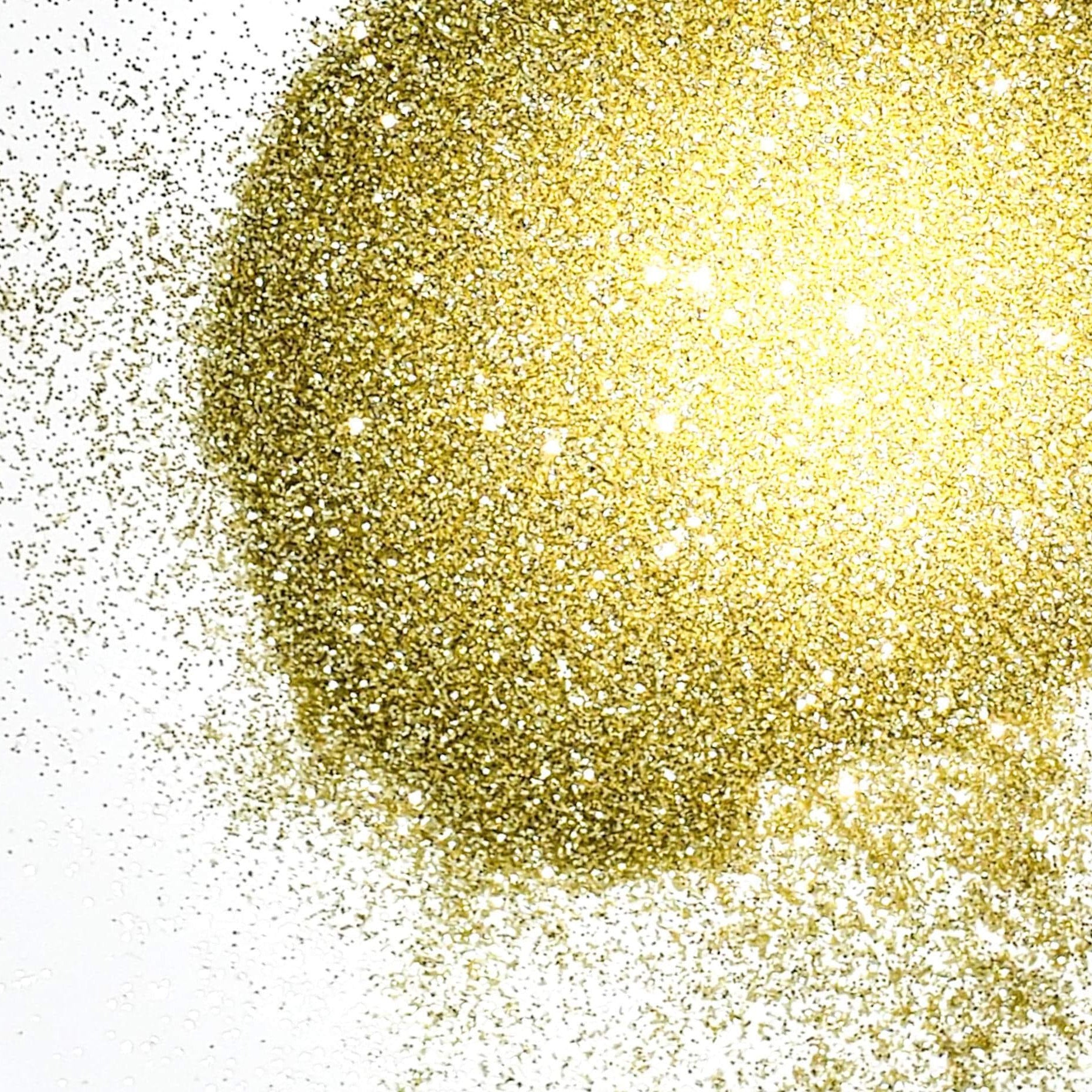 A close-up image of extra fine gold glitter spread on a white background, resembling the appearance of sandy glitter.