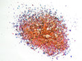 A pile of orange irregular glitter flakes spread out on a white background.