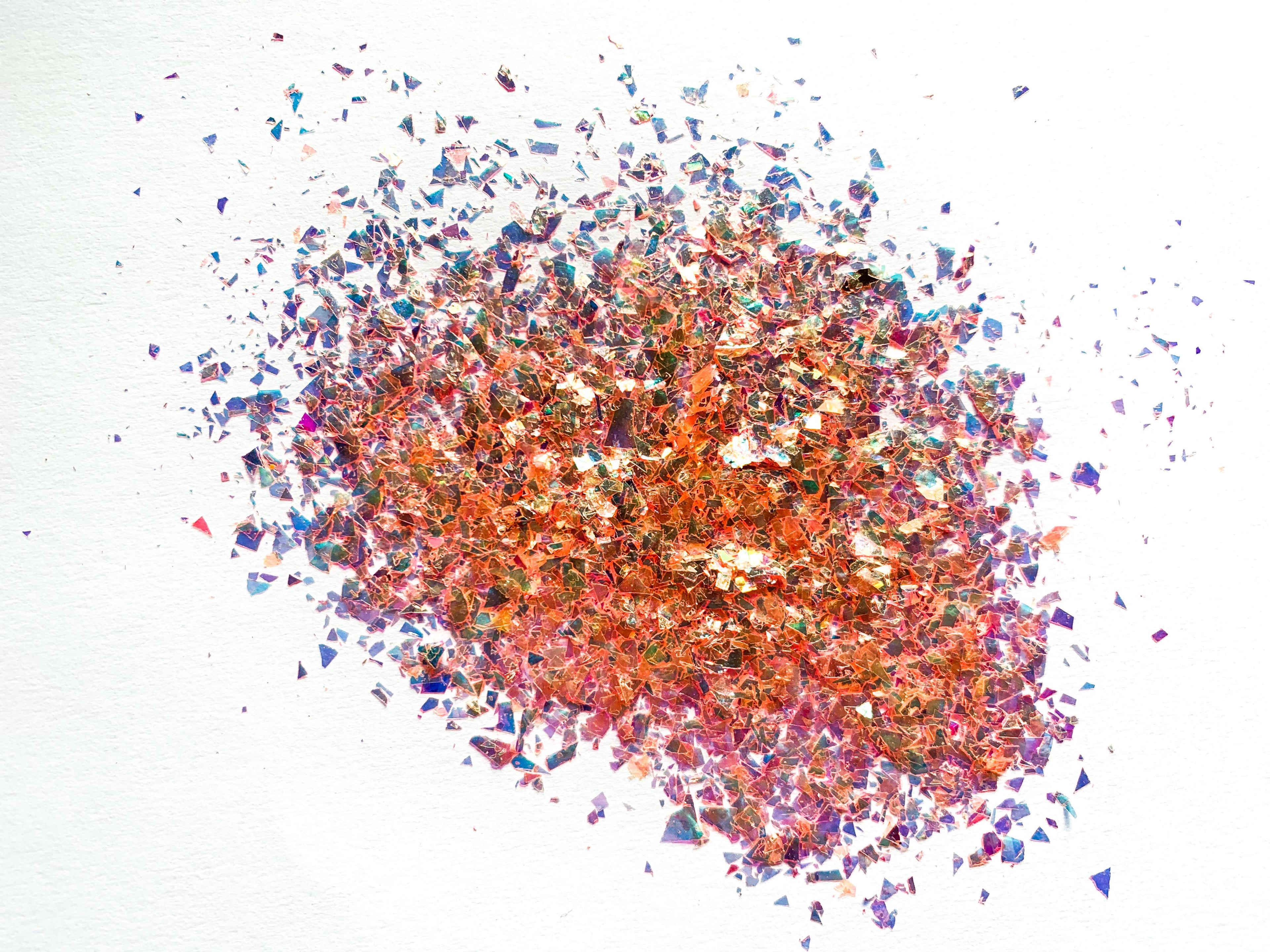 A pile of orange irregular glitter flakes spread out on a white background.