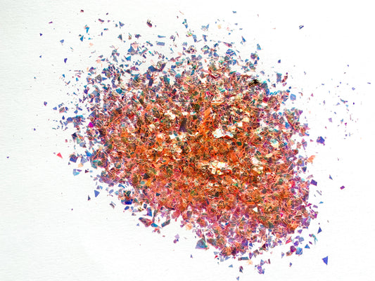 A pile of orange irregular glitter flakes spread out on a white background.