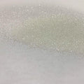 A close-up image of white glitter spread out on a surface, showing the texture and sparkle of the product.
